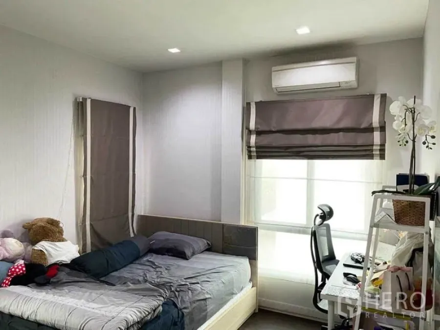 Detached House for sale in Prawet, Bangkok - Bright bedroom with double bed, study desk, air conditioner and grey roman blinds.