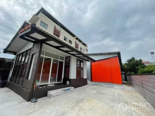 Warehouse for rent in Khlong Toei, Bangkok - Modern office building with large windows beside a bright orange sliding warehouse door.