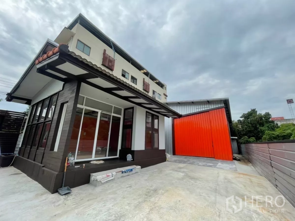 Warehouse for rent in Khlong Toei, Bangkok - Modern office building with large windows beside a bright orange sliding warehouse door.