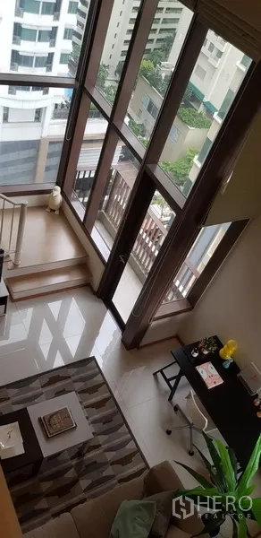 Condominium for rent in Khlong Toei, Bangkok - Double-height windows in the living room offering city views and balcony access.