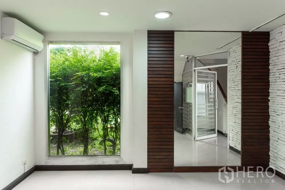 Home Office for rent in Lat Phrao, Bangkok - Room with a large window facing a green hedge and wood slat accent wall.