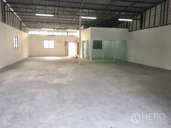 Warehouse for rent in Lam Luk Ka, Pathum Thani - Spacious storage hall showing metal trusses, ventilation windows and a glass-partitioned office within the warehouse.