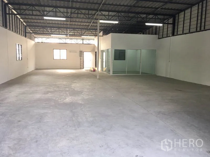 Warehouse for rent in Lam Luk Ka, Pathum Thani - Spacious storage hall showing metal trusses, ventilation windows and a glass-partitioned office within the warehouse.