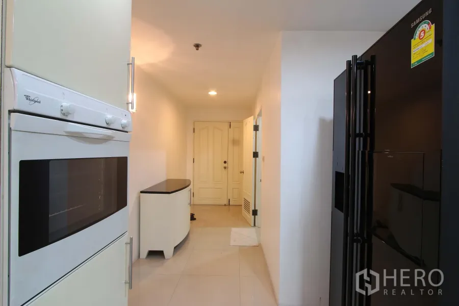 Condominium for rent in Watthana, Bangkok - Bright galley kitchen corridor with built-in oven, large black fridge, and hallway to the entry door in a Bangkok condo.