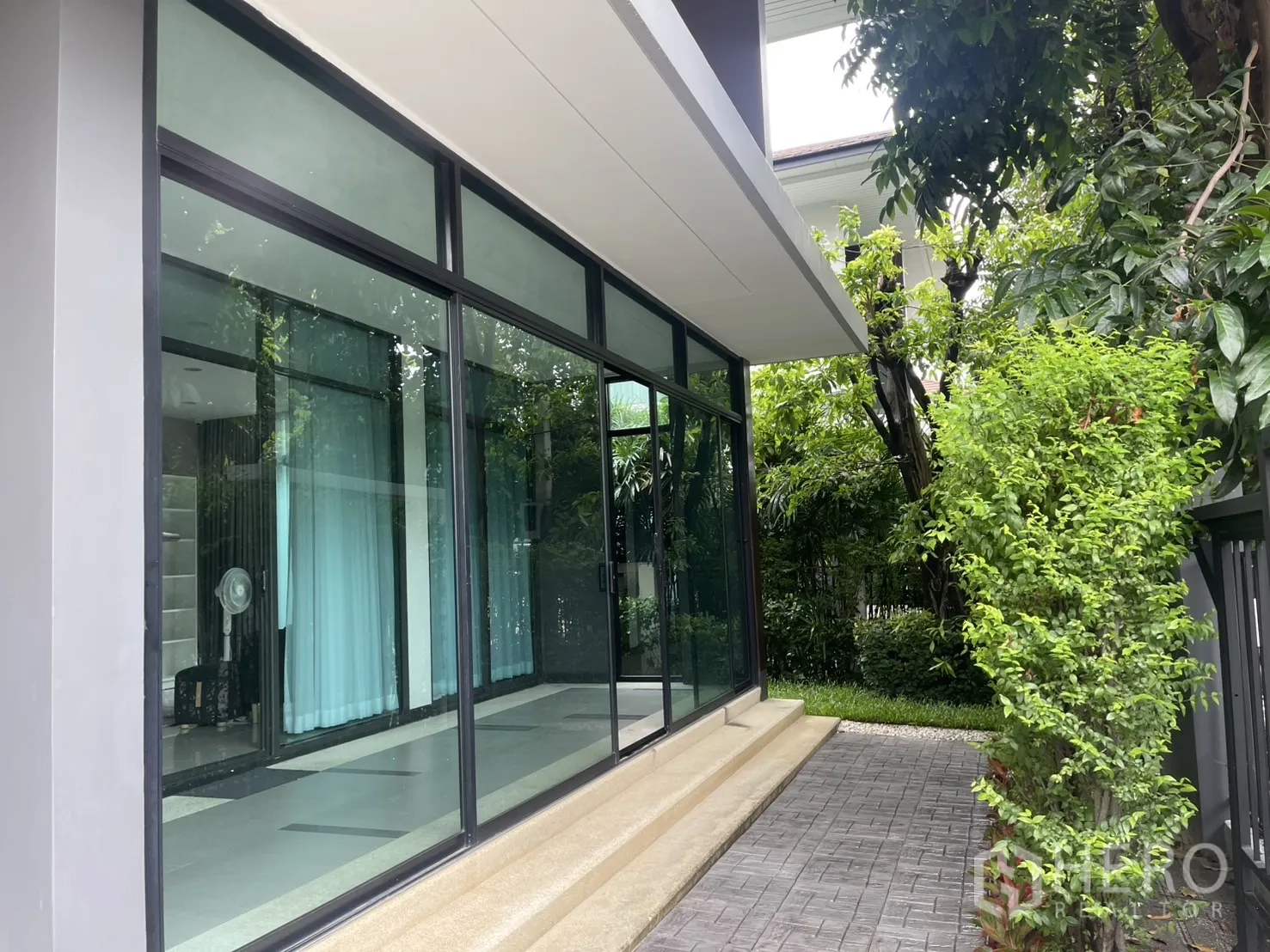 Detached House for rent in Bang Kapi, Bangkok - Exterior side of the house with large glass panels and shrub-lined path.