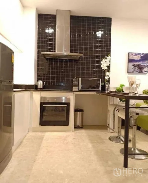 Condominium for rent in Khlong Luang, Pathum Thani - Modern L-shaped kitchen with black tile backsplash, oven and range hood.