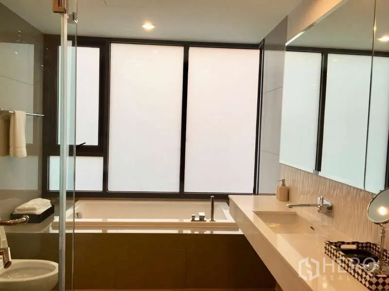 Condominium for rent in Khlong Toei, Bangkok - Bathroom with soaking tub, separate glass shower and long vanity by frosted windows.