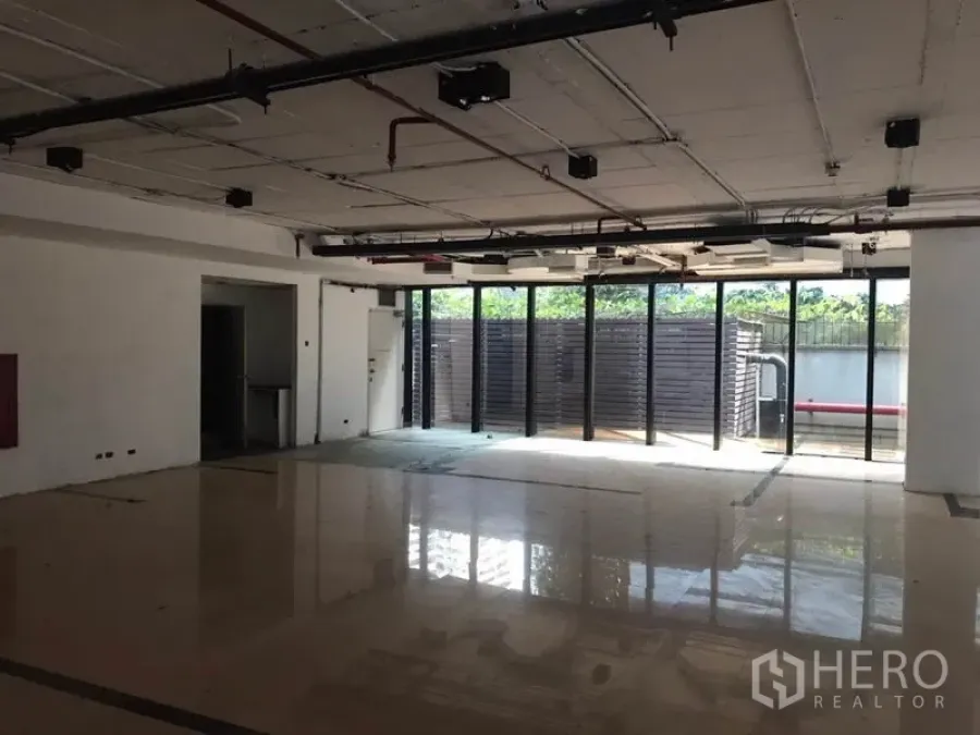 Office Space for rent in Watthana, Bangkok - Open-plan office with polished floors, exposed ceiling services, and full-height glass opening to a private outdoor area.
