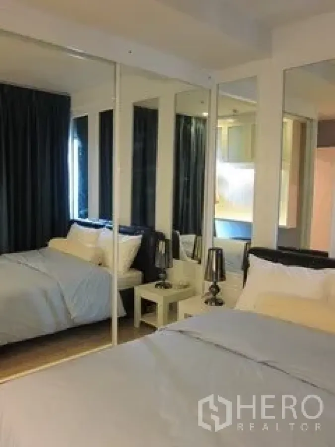 Condominium for rent in Khlong Toei, Bangkok - Cozy bedroom with mirrored wardrobe, dark curtains and bedside lamps.