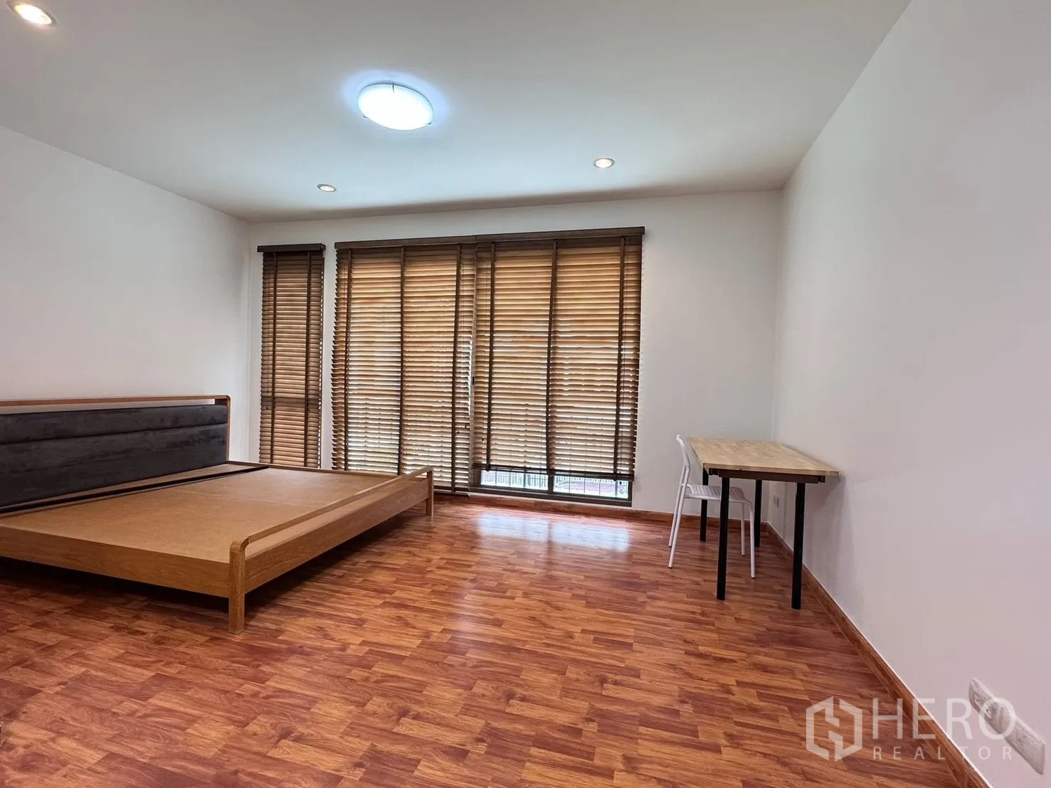 Townhouse for rent in Phra Khanong, Bangkok - Spacious bedroom with wood floors, desk, and wide window blinds.