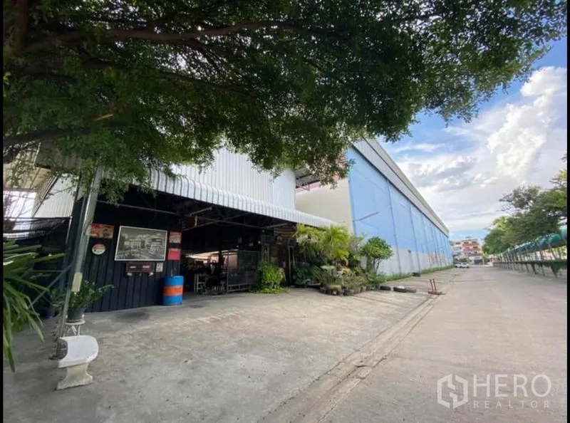 คลังสินค้า ให้เช่าในSai Mai, Bangkok - ทางเข้าโกดังมีหลังคาเมทัลชีท พื้นที่ออฟฟิศย่อย และลานคอนกรีตร่มรื่นด้วยต้นไม้ใหญ่