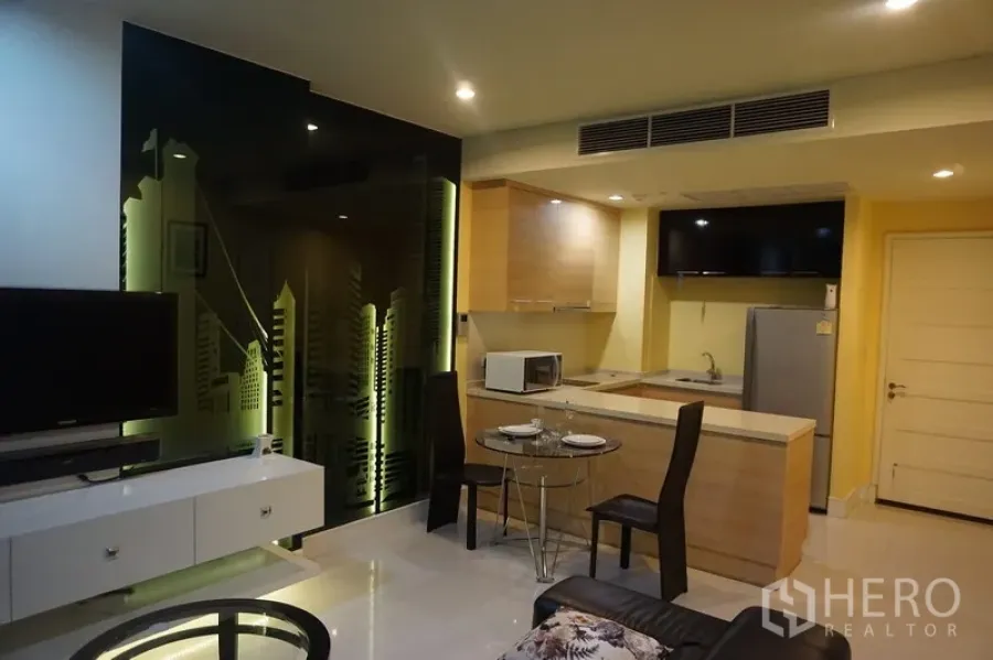 Condominium for sale in Khlong Toei, Bangkok - Open‑plan living room with TV console, black glass skyline feature wall, and fitted kitchenette in a Khlong Toei Bangkok condo.