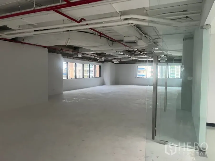 Office Space for rent - Open office seen from the glass doorway, showing ceiling services and unfinished concrete floor.