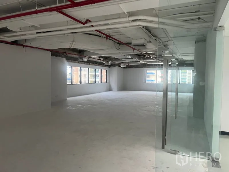 Office Space for rent - Open office seen from the glass doorway, showing ceiling services and unfinished concrete floor.