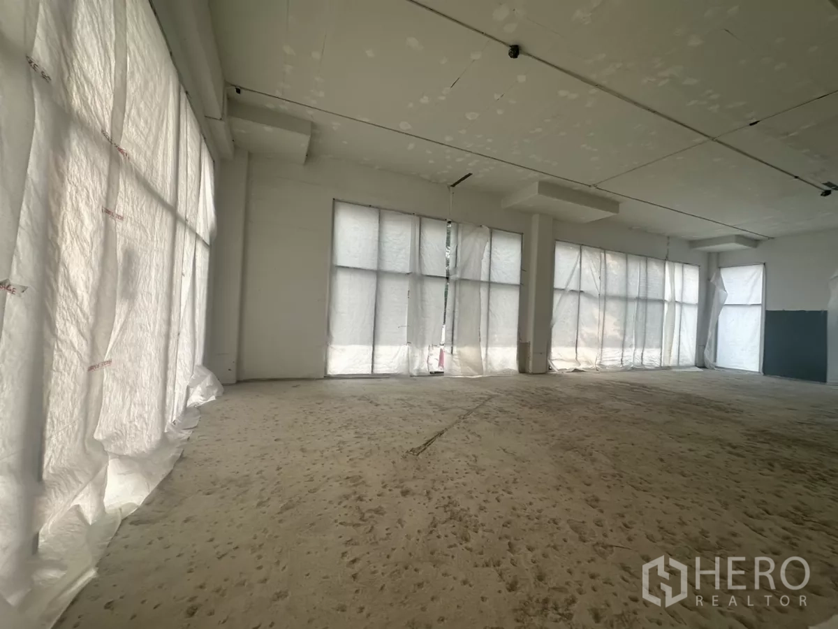 Retail Space for rent in Khlong Toei, Bangkok - Spacious empty unit with multiple full-height windows, white walls and ample natural light.
