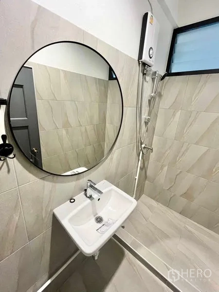 Home Office for rent in Khlong Toei, Bangkok - Compact bathroom with round mirror, white basin and shower heater.