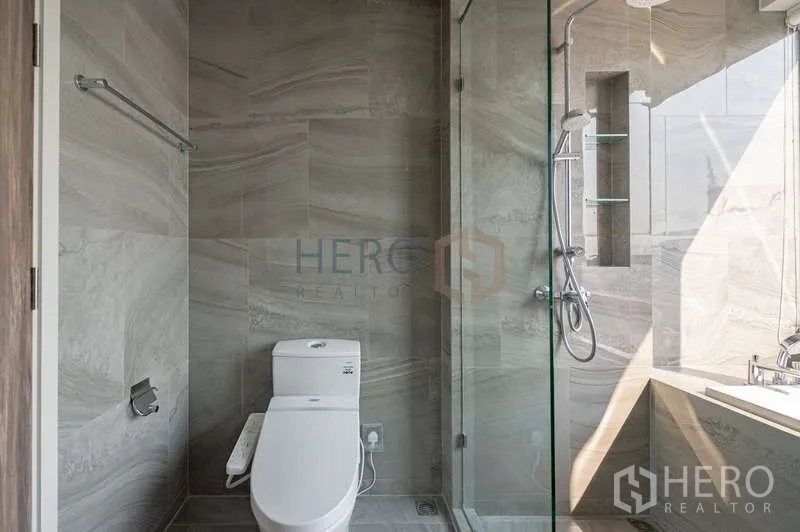 Condominium for rent - Modern bathroom with glass shower, toilet and a bathtub ledge in gray stone tiles.
