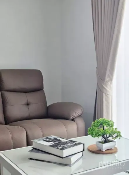 Townhouse for rent in Bang Phli, Samut Prakan - Cozy corner featuring a brown recliner, coffee table with books and floor-length curtains.