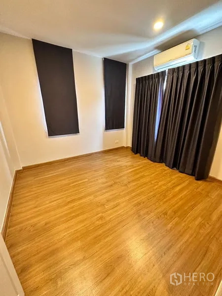 Detached House for sale in Prawet, Bangkok - Empty bedroom with wood floor, blackout curtains and wall air conditioner.