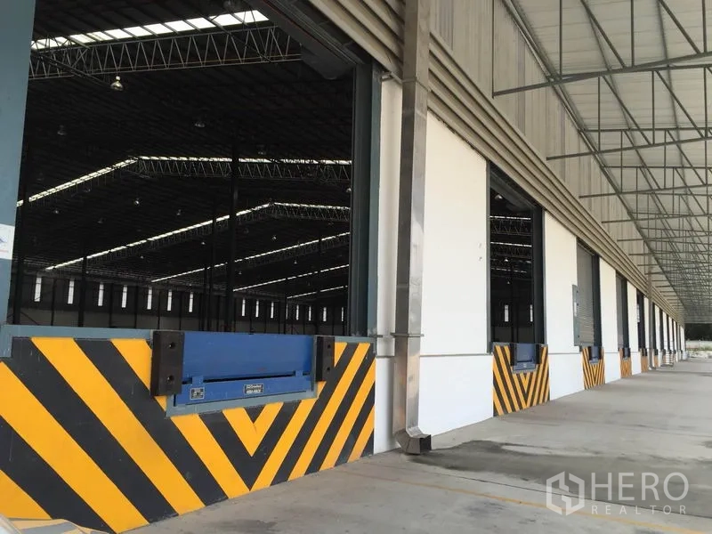 Warehouse for rent in Si Racha, Chon Buri - Loading bay with dock leveler and yellow-black bumpers along a covered raised platform.
