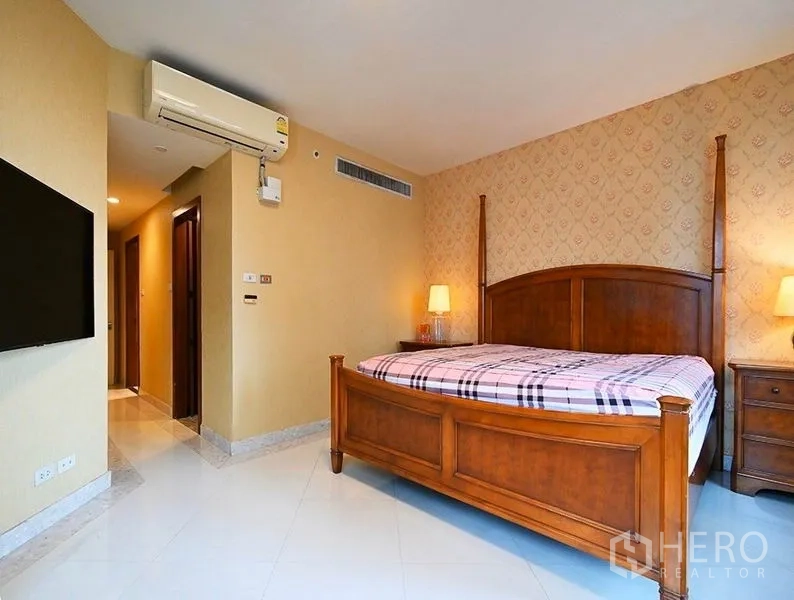 Condominium for rent in Pathum Wan, Bangkok - Spacious master bedroom with wooden bed frame, warm wallpaper, bedside tables, and soft lighting.