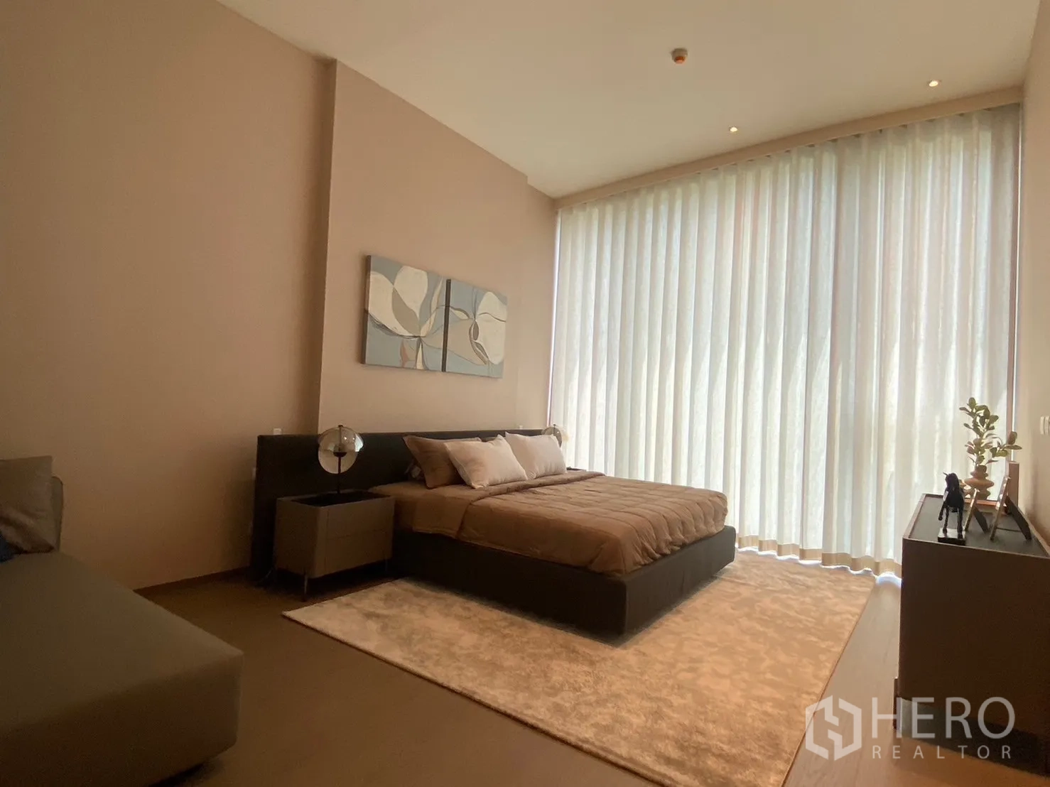 Condominium for rent in Pathum Wan, Bangkok - Spacious bedroom with floor-to-ceiling sheer curtains, king bed, bedside tables, rug, and modern console.