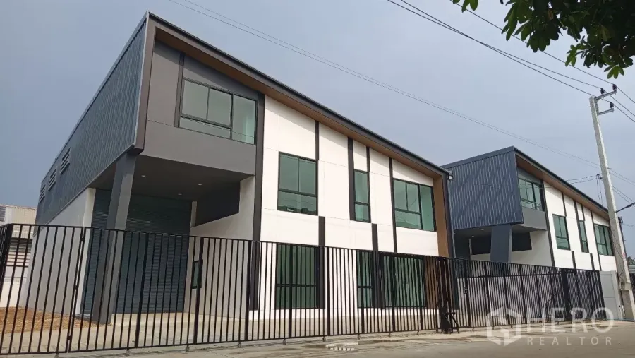 Warehouse for rent or sale in Lam Luk Ka, Pathum Thani - Modern warehouse units with sloped roofs and tall windows behind a black metal fence in Lam Luk Ka.