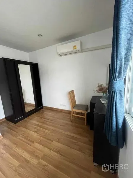 Townhouse for rent in Suan Luang, Bangkok - Bright bedroom with wood floor, wardrobe, dressing table and window with blue curtains.