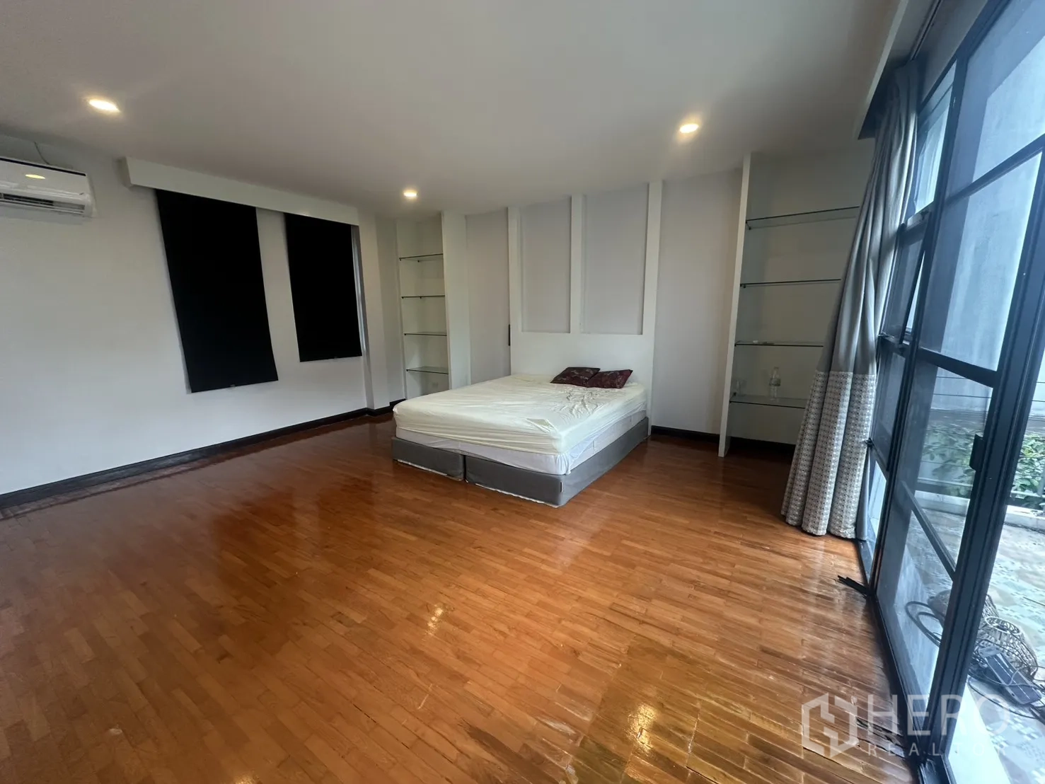 Detached House for rent in Watthana, Bangkok - Spacious bedroom with wood flooring, bed, air conditioner, and built-in shelves.