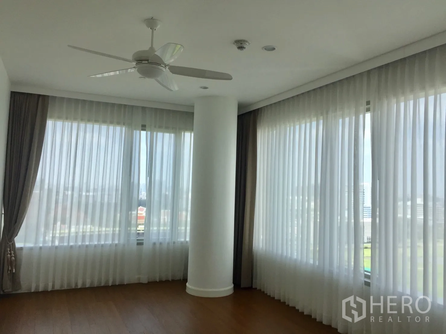 Condominium for rent in Pathum Wan, Bangkok - Corner living area with floor-to-ceiling windows, sheer curtains and ceiling fan.