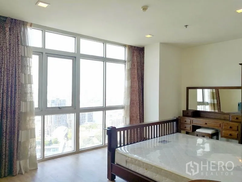 Condominium for rent in Khlong Toei, Bangkok - Bedroom with full-height corner windows, wood bed and vanity.