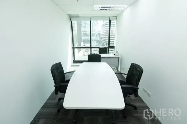 Office Space for rent - Compact meeting room with an oval table, three chairs and a window facing high-rise buildings.