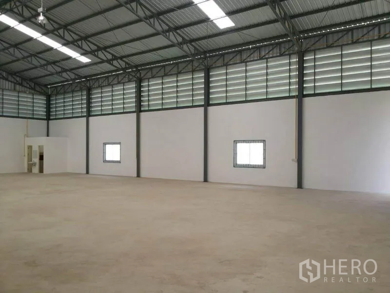 Warehouse for rent in Lam Luk Ka, Pathum Thani - Open storage hall showing ventilation panels, small windows, and a built‑in bathroom area.