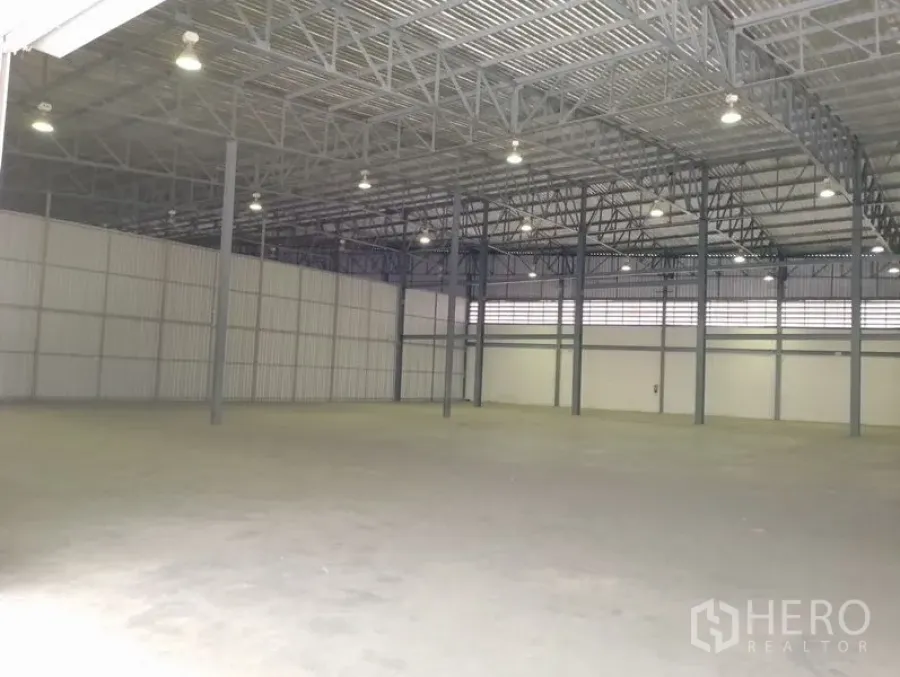 Warehouse for rent in Bang Phli, Samut Prakan - Spacious warehouse interior with high-clearance steel truss roof, bright high-bay lights, and smooth concrete floor.