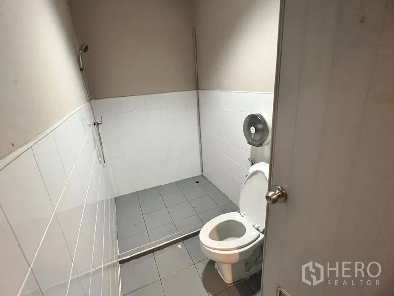 Warehouse for rent in Suan Luang, Bangkok - Simple restroom with tiled walls, toilet and a shower area.
