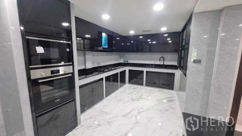 Townhouse for rent in Khlong Toei, Bangkok - Contemporary built-in kitchen with black cabinetry, oven stack, and marble-look floor.