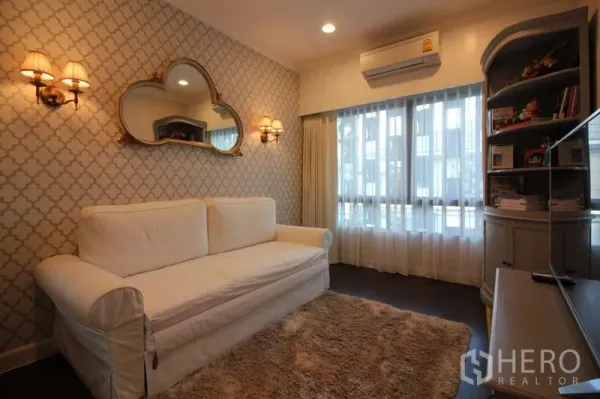 Detached House for rent in Prawet, Bangkok - Cozy sitting room with a white sofa, patterned wallpaper and warm wall sconces.