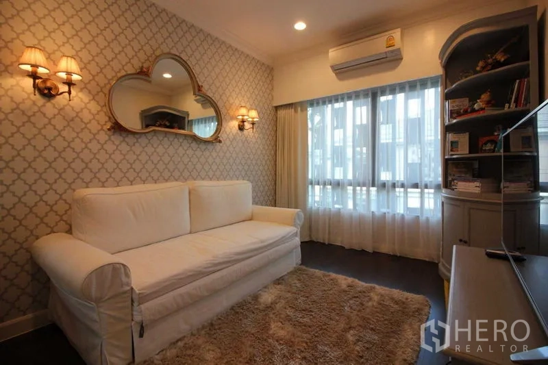 Detached House for rent in Prawet, Bangkok - Cozy sitting room with a white sofa, patterned wallpaper and warm wall sconces.