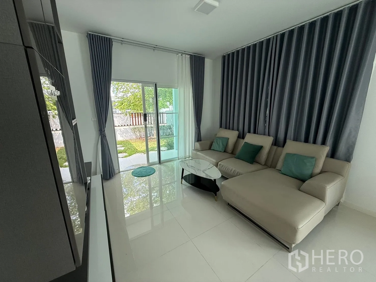 Detached House for rent in Bang Phli, Samut Prakan - Living room with sliding glass doors opening to the garden and full-length curtains.