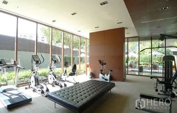 Condominium for rent in Khlong Toei, Bangkok - Fitness room with treadmills, exercise bikes and garden views through floor-to-ceiling glass.