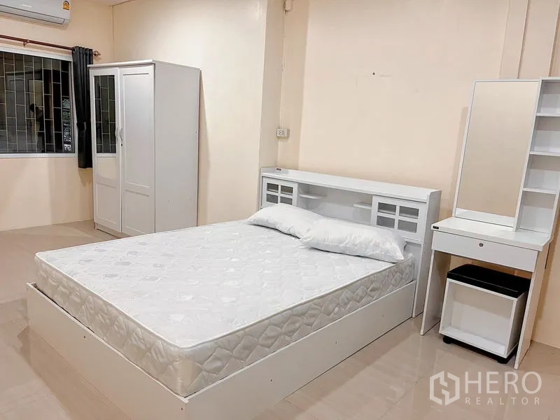 Townhouse for rent in Huai Khwang, Bangkok - Airy second bedroom with white furniture, wardrobe and curtained window.