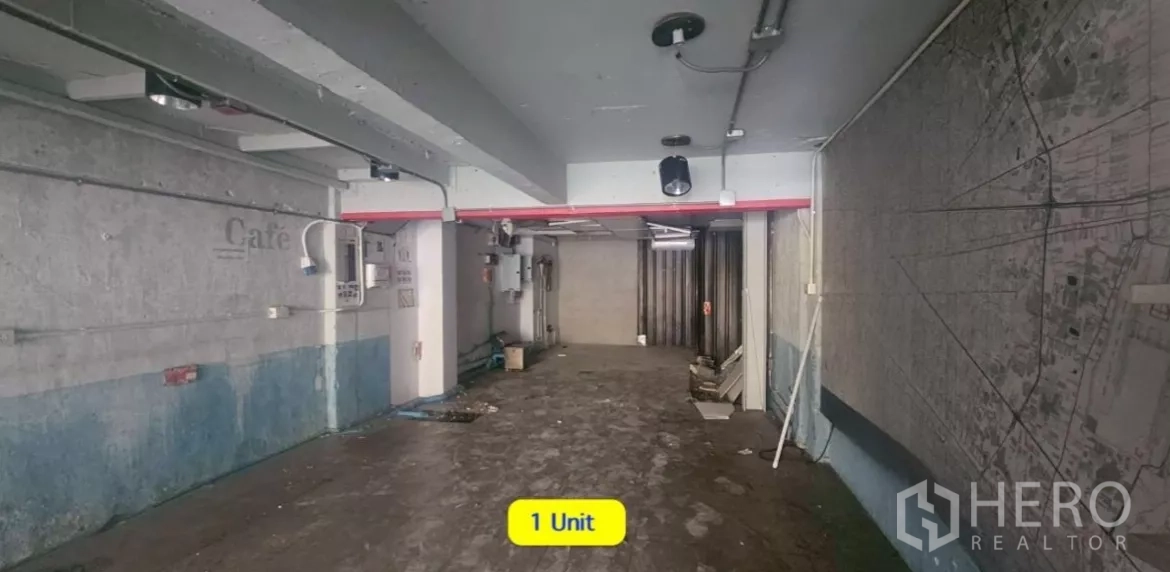 Shophouse for rent in Watthana, Bangkok - Open-plan ground floor of a shophouse with concrete floor, exposed conduits, and a metal shutter.