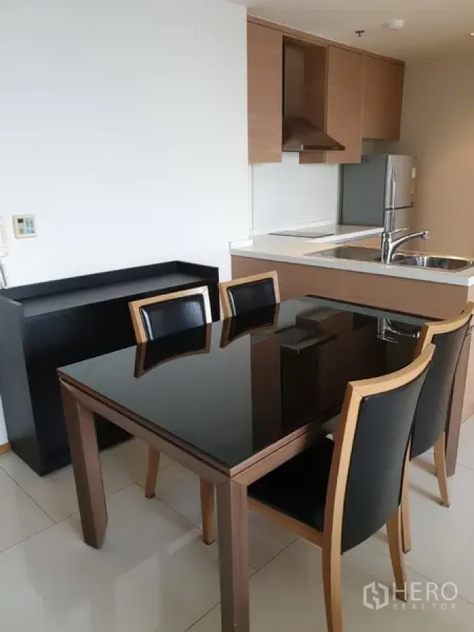Condominium for rent in Khlong Toei, Bangkok - Open-plan kitchen with wood cabinets, stainless sink, fridge and a glossy black dining table for four.