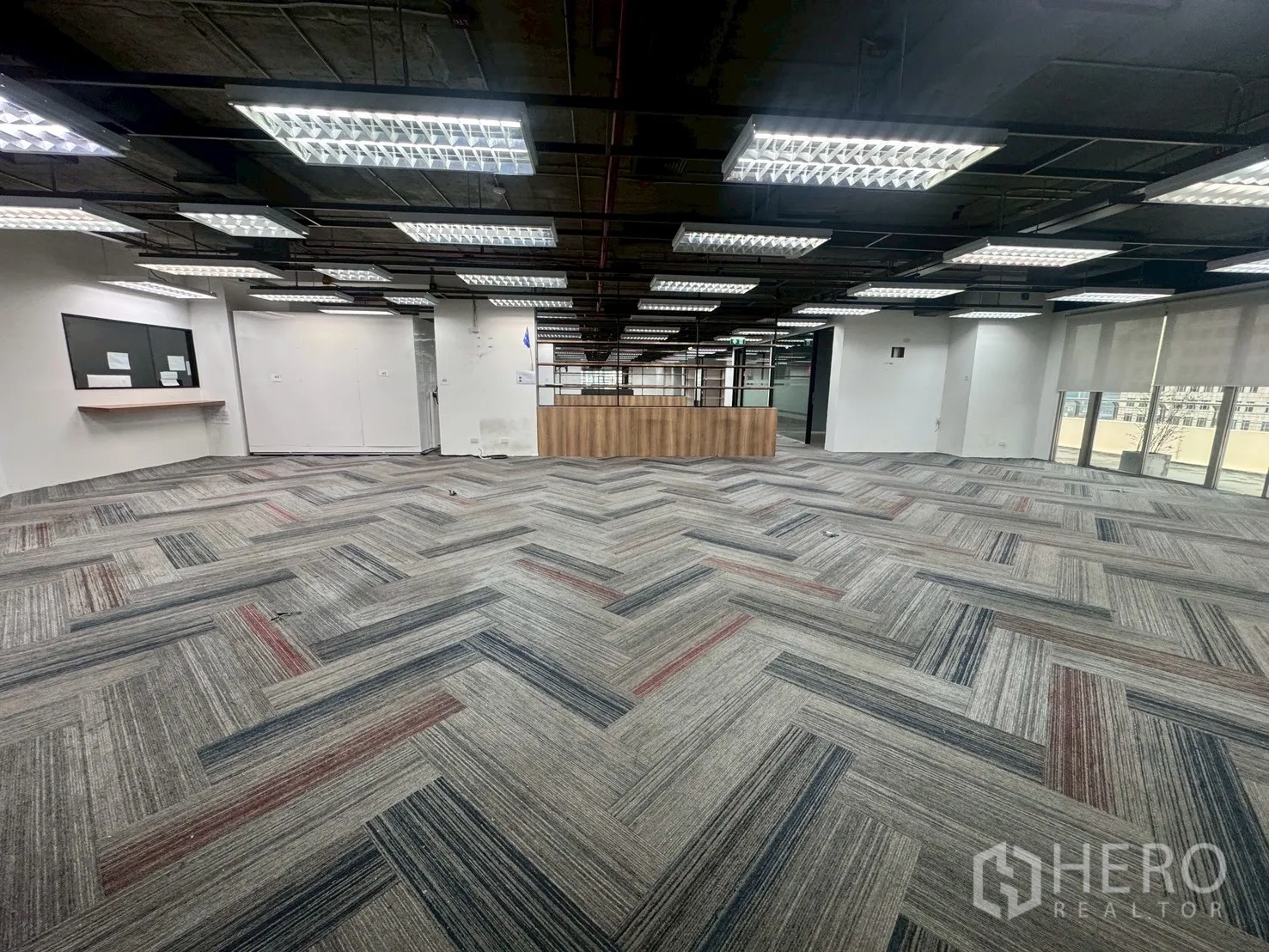 Office Space for rent in Watthana, Bangkok - Large workspace with patterned carpet, bright ceiling light panels, and a wood service counter at the center.