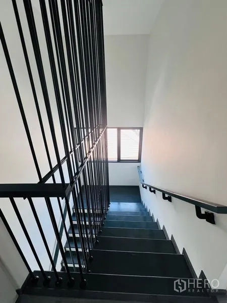 Home Office for sale in Bang Khen, Bangkok - Close view of a staircase with vertical black railings and a window bringing in daylight.