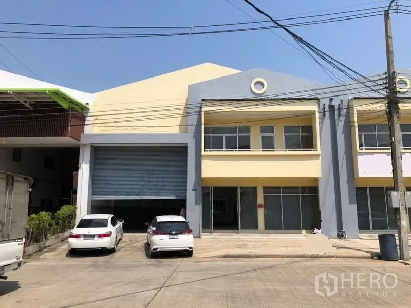 工厂 出租在Khlong Luang, Pathum Thani - 两层厂房外观，宽大卷闸门、停车位与进出车道。