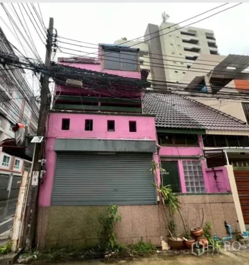 店屋 出租在Watthana, Bangkok - 瓦他那区粉色多层店屋外观，临街卷闸门与瓦屋顶。