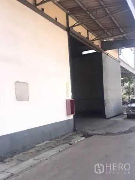 Warehouse for rent in Chachoengsao - Side entrance to warehouse with tall sliding door and wall-mounted fire cabinet under a roofed bay.