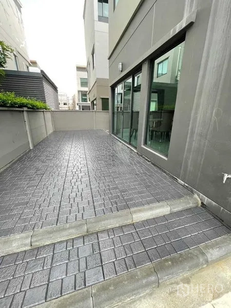 Detached House for rent in Khan Na Yao, Bangkok - Paved side terrace beside a modern three‑storey house with sliding glass doors.