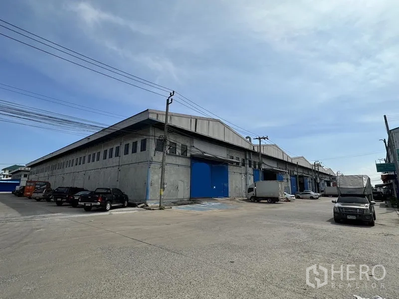 Warehouse for rent in Bang Phli, Samut Prakan - Corner exterior of a large concrete warehouse with blue loading doors and ample driveways in Bang Phli, Samut Prakan.
